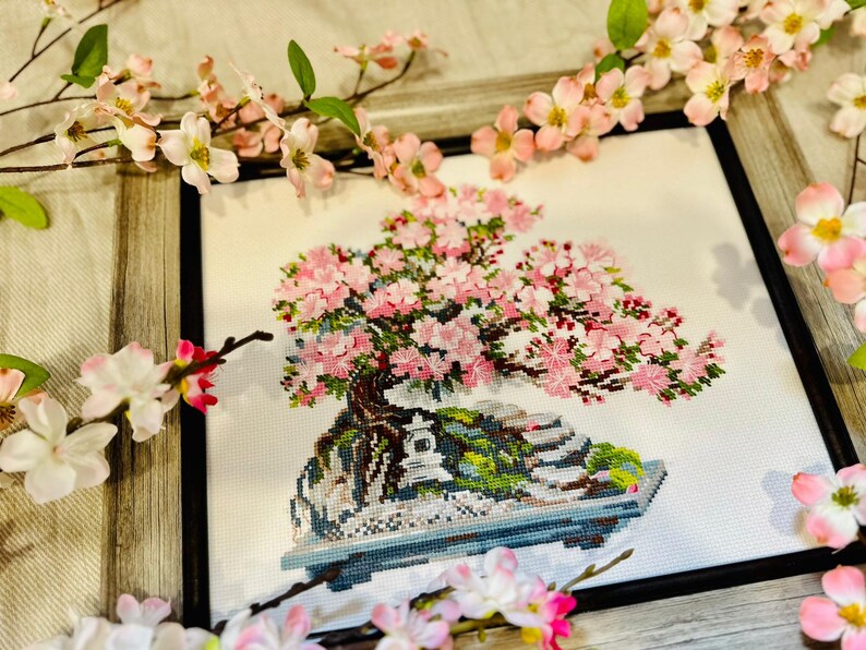 The RIOLIS cross stitch kit Flowering Bonsai features a delicate bonsai design using 17 colors of wool/acrylic threads. The kit includes a needle, Zweigart 14ct white AIDA fabric, and a color chart. The finished size is 30x24 cm (11¾in x 9½in).