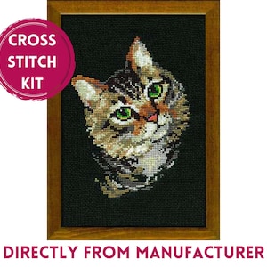 May include: A cross stitch kit featuring a tabby cat with green eyes on a black background, framed in a brown wooden frame. A pink circular badge on the top left reads CROSS STITCH KIT, and text at the bottom reads DIRECTLY FROM MANUFACTURER.