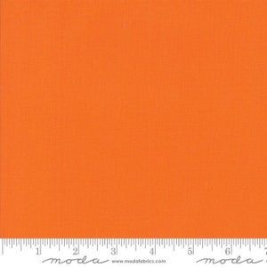 May include: Solid orange fabric swatch with a ruler showing 7 inches. The ruler has the word "moda" printed on it.