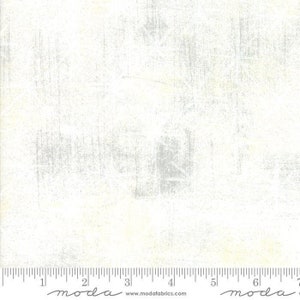 May include: White fabric with a distressed, textured appearance. The fabric has a subtle, mottled pattern with vertical and horizontal streaks in shades of gray. A ruler is along the bottom edge, with the word "moda" printed on it.