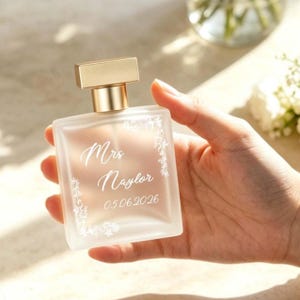 May include: A square frosted glass perfume bottle with a gold-coloured cap. The bottle is inscribed with the words "Mrs Naylor" and the date "05.06.2026" in a decorative script, with floral embellishments.