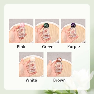 May include: Five small, clear glass bottles with colored spherical stoppers. The stoppers are pink, green, purple, white, and brown. Each bottle is labeled with its corresponding color name: Pink, Green, Purple, White, and Brown.