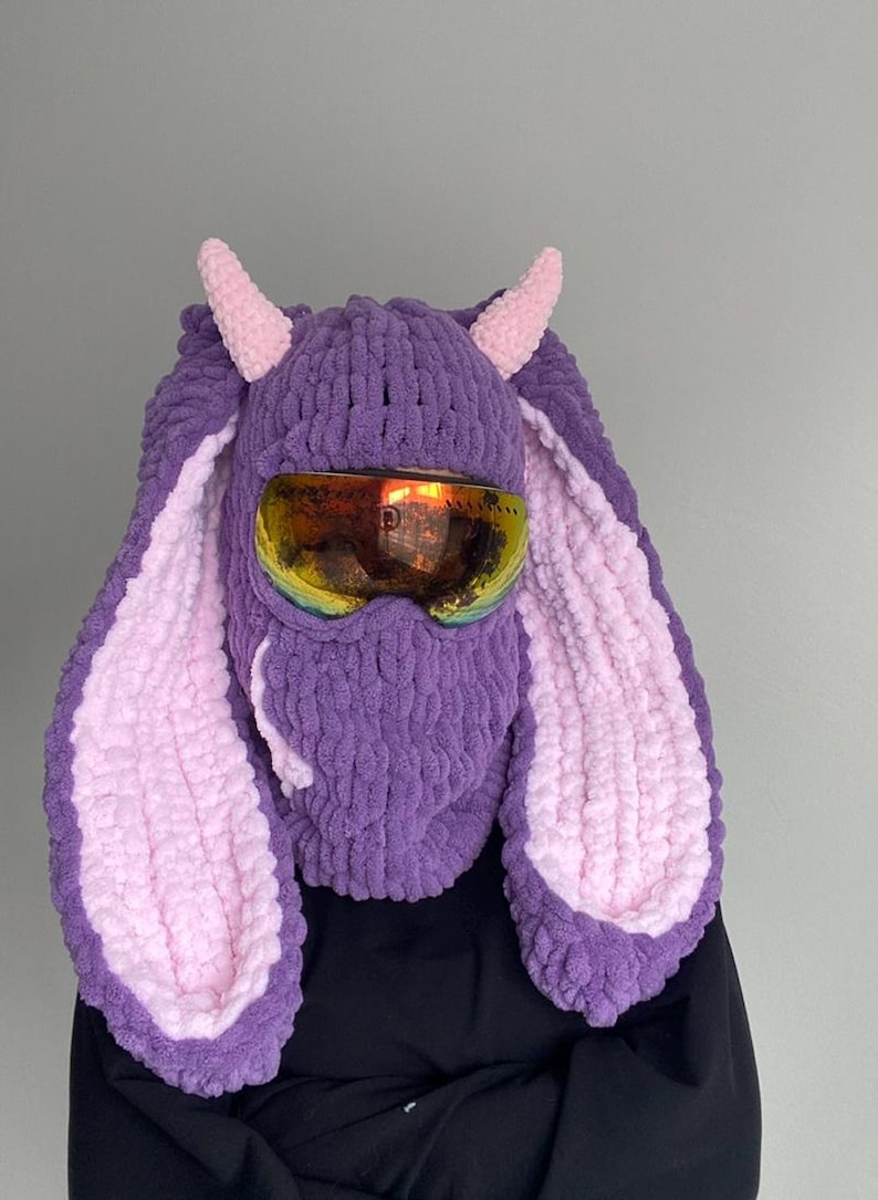 Puede incluir: M&aacute;scara de esqu&iacute; de punto morado y rosa con orejas de conejo largas y gafas de esqu&iacute;.
