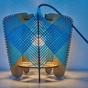 Könnte beinhalten: Eine blaue und hölzerne Pendelleuchte mit einem gewebten blauen Schirm. Die Lampe ist eingeschaltet und beleuchtet den Raum.