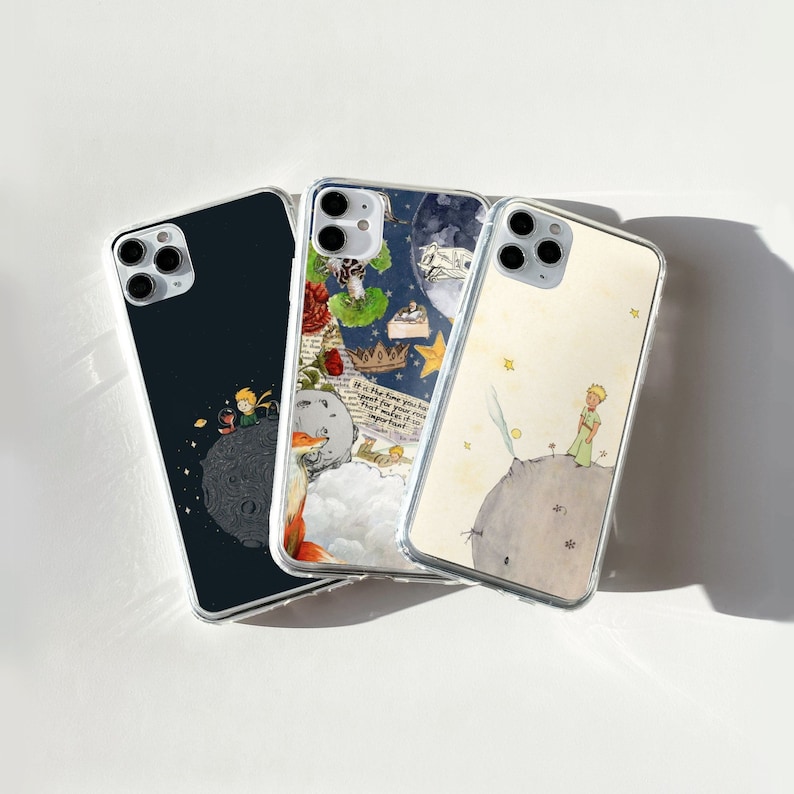 Puede incluir: Tres fundas transparentes para tel&eacute;fono con ilustraciones de "El Principito". Una funda tiene un fondo azul oscuro con el Principito en un planeta. Otra presenta un collage de im&aacute;genes. La tercera muestra al Principito en un peque&ntilde;o planeta con estrellas.