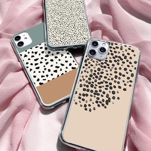 Può includere: Tre custodie per telefono trasparenti con diversi motivi a pois neri e bianchi. Le custodie sono su uno sfondo di tessuto rosa.