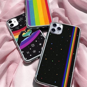 Puede incluir: Tres fundas para teléfono con diseños coloridos. Una funda presenta un arcoíris, otra tiene un arcoíris y estrellas, y la tercera tiene un fondo negro con una franja de arcoíris y estrellas de colores. Las fundas tienen bordes transparentes.