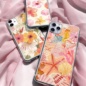May include: Three clear phone cases with different designs. The first case has a floral pattern with pink and yellow flowers. The second case has a tropical floral pattern with orange and yellow flowers. The third case has a sea life pattern with coral, starfish, and a seahorse.