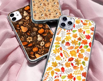Puede incluir: Tres fundas transparentes para teléfono con diseños otoñales. Una funda presenta un patrón de hojas de otoño rojas, naranjas y amarillas. Otra tiene un fondo marrón con calabazas y calabazas. La tercera funda tiene un fondo beige con pájaros y hojas.