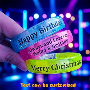 May include: Three translucent silicone wristbands in blue, pink, and yellow. The blue band features the text Happy Birthday, the pink band reads Always and Forever Walter & Brittany, and the yellow band displays the text Merry Christmas.