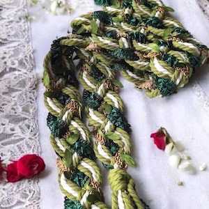 Può includere: Una corda intrecciata verde e bianca con foglie verdi intrecciate nella treccia. La corda ha nappe alle estremità.