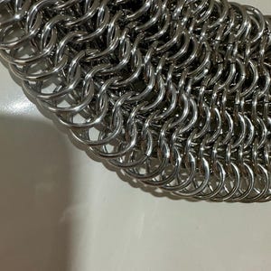 May include: Close-up of a silver chainmail, a type of armor made of interlocking metal rings.
