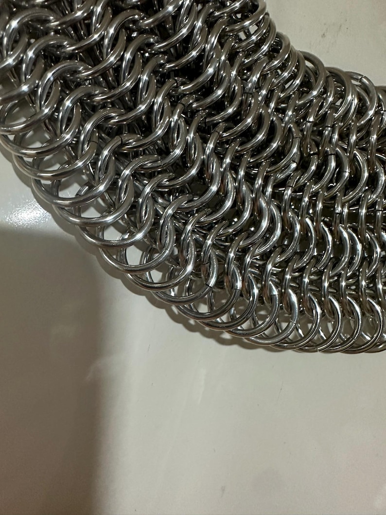 May include: Close-up of a silver chainmail, a type of armor made of interlocking metal rings.