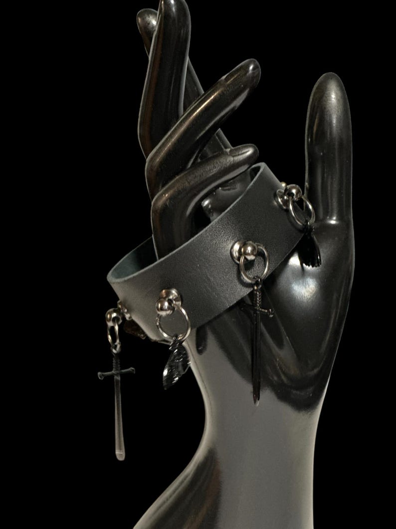 May include: Black leather bracelet with silver metal accents and dangling sword charms.