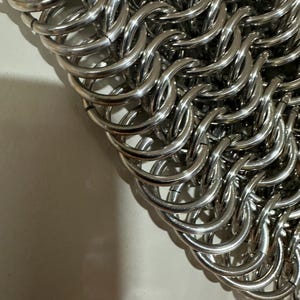 May include: A close-up of a silver chainmail bag made of interlocking metal rings.