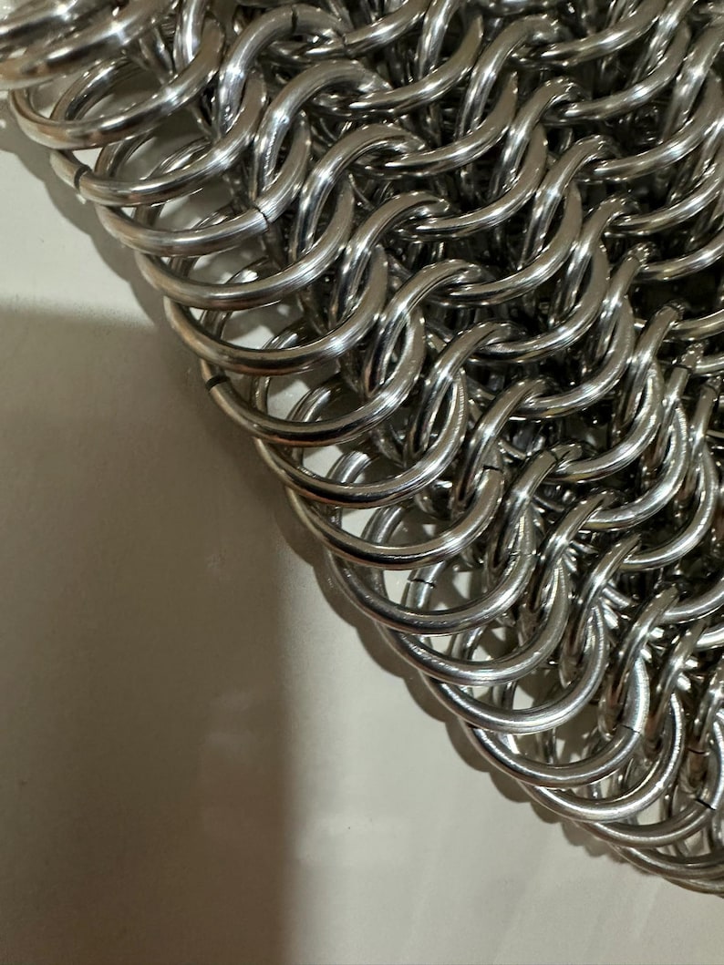 May include: A close-up of a silver chainmail bag made of interlocking metal rings.