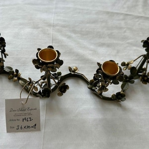 Puede incluir: Un candelabro decorativo de metal con cuatro candeleros. El candelabro tiene forma de vid con hojas y flores. Los candeleros son de color dorado. Las dimensiones son 91 x 25 x 20 cm.