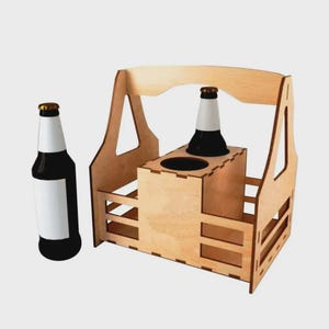 Puede incluir: Un portabotellas de madera con asa, diseñado para dos botellas. El portabotellas es de madera clara y tiene una base rectangular con detalles recortados. Una botella de cerveza con etiqueta blanca y una botella negra están junto al portabotellas.