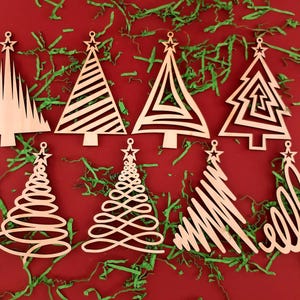 Può includere: Una collezione di otto ornamenti per l'albero di Natale in legno con vari disegni, tra cui motivi geometrici e a spirale. Ogni ornamento ha una stella in cima ed è esposto su uno sfondo rosso con carta verde sminuzzata.