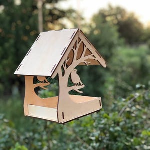 May include: A wooden bird feeder with a roof and a cutout design of a tree with birds. The feeder has a rectangular tray for birdseed.