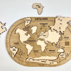 Può includere: Puzzle di mappa del mondo in legno con continenti ritagliati, tra cui Nord America, Sud America, Africa, Europa, Asia e Antartide. La mappa è incisa con testo in russo e presenta una finitura marrone chiaro.