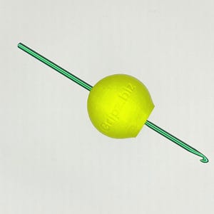 May include: A lime green crochet hook with a neon yellow grip. The grip has the text "gripz.biz" printed on it. The hook is angled and set against a white background.