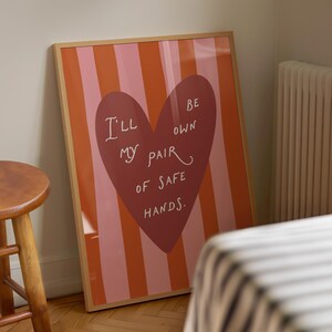 Pu&ograve; includere: Stampa artistica incorniciata con sfondo a righe verticali rosa e arancioni. Un grande cuore bordeaux al centro contiene il testo scritto a mano: "I'll be my own pair of safe hands."