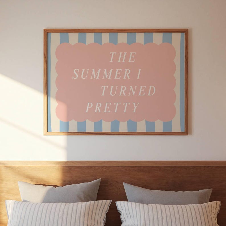 May include: A framed art print with the text "THE SUMMER I TURNED PRETTY" in white on a pink cloud-shaped background. The frame is wood, and the background has blue and white stripes.