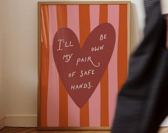 May include: A framed art print with a wooden frame. The artwork features a large maroon heart with the words "I'll be my own pair of safe hands" in white. The background has vertical stripes of pink and orange.