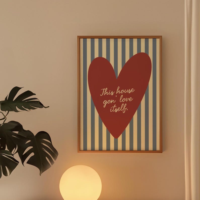 May include: Framed wall art featuring a red heart on a striped background of blue and beige. The text "This house gon' love itself" is written in cursive. The artwork is in a wooden frame.