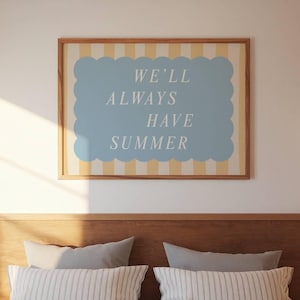 Pode incluir: Uma impressão de arte emoldurada com o texto "WE'LL ALWAYS HAVE SUMMER" em branco sobre uma forma ondulada azul clara. O fundo tem listras verticais amarelas e brancas, e a moldura é de madeira.