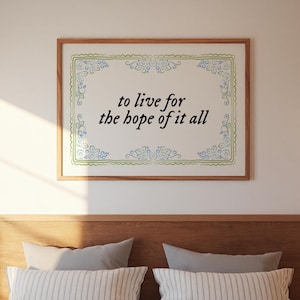 May include: A framed print with the text "to live for the hope of it all." The print has a light background with a decorative green and blue border. The frame is made of wood and is hanging above a bed.