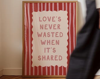 May include: A framed art print with the text "LOVE'S NEVER WASTED WHEN IT'S SHARED." The background features red and pink vertical stripes. The text is in a serif font and is in a light red color. The frame is a light brown color.