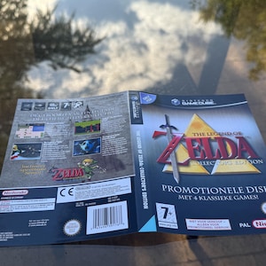 Può includere: Una copertina per gioco Nintendo GameCube di The Legend of Zelda: Collector's Edition. Il fronte presenta il titolo del gioco, una spada e un triangolo dorato. Il retro mostra screenshot, descrizioni del gioco, un codice a barre e il marchio Nintendo.