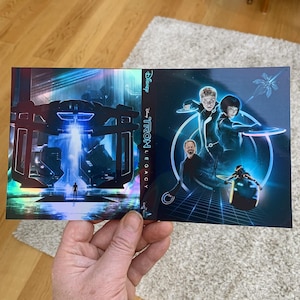 May include: A promotional item for the movie "Tron: Legacy" featuring a futuristic cityscape and characters in neon blue and black suits. The Disney logo is visible.