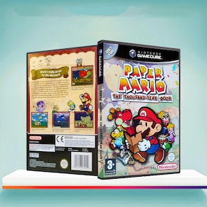 Puede incluir: Dos cajas de juego para el juego de Nintendo GameCube "Paper Mario: The Thousand-Year Door". La caja frontal presenta a Mario y otros personajes. La caja trasera tiene detalles del juego y capturas de pantalla. Las cajas están sobre una superficie blanca.