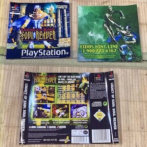 May include: Legacy of Kain: Soul Reaver PlayStation game cover art and manual inserts. The front cover features the main character, while the back displays game screenshots, text, a barcode, and the Eidos hint line phone number 1-900-773-4367.