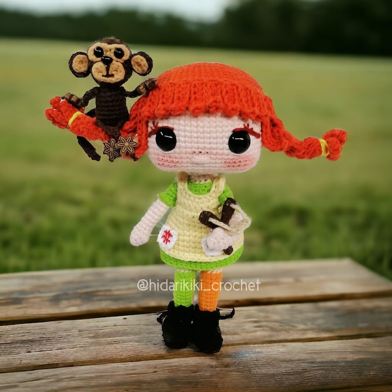 May include: A handmade crochet doll with red pigtails and a small monkey perched on her head. The doll wears a green and yellow dress, black boots, and orange and green striped socks. The doll is holding a small object in her hands. The doll is sitting on a wooden surface.