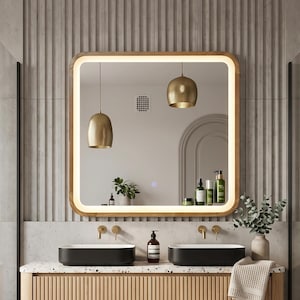 Peut inclure: Un miroir de salle de bain mural carré aux coins arrondis avec une bande lumineuse LED intégrée le long du cadre intérieur. Le miroir présente une bordure en bois clair et un petit bouton d'alimentation lumineux sur le côté inférieur droit.