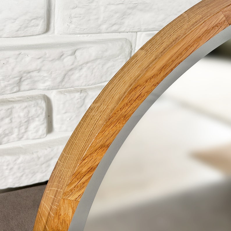 May include: A circular mirror featuring a light brown natural wood frame with a visible grain pattern. The frame has a smooth, rounded edge that curves inward toward the reflective glass surface, showcasing the texture of the wood material.