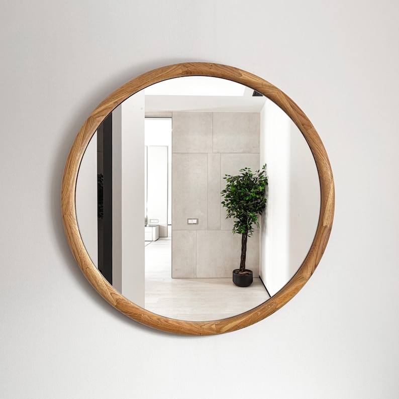 May include: A round mirror with a natural wood frame. The mirror reflects a room with a plant in a pot.