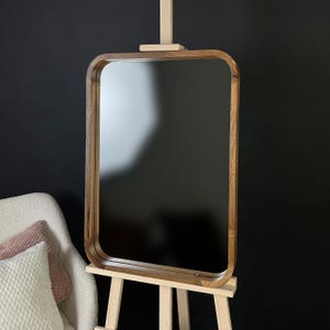 Peut inclure: Un miroir encadré en bois avec des bords arrondis, posé sur un chevalet. Le miroir reflète l'environnement environnant.