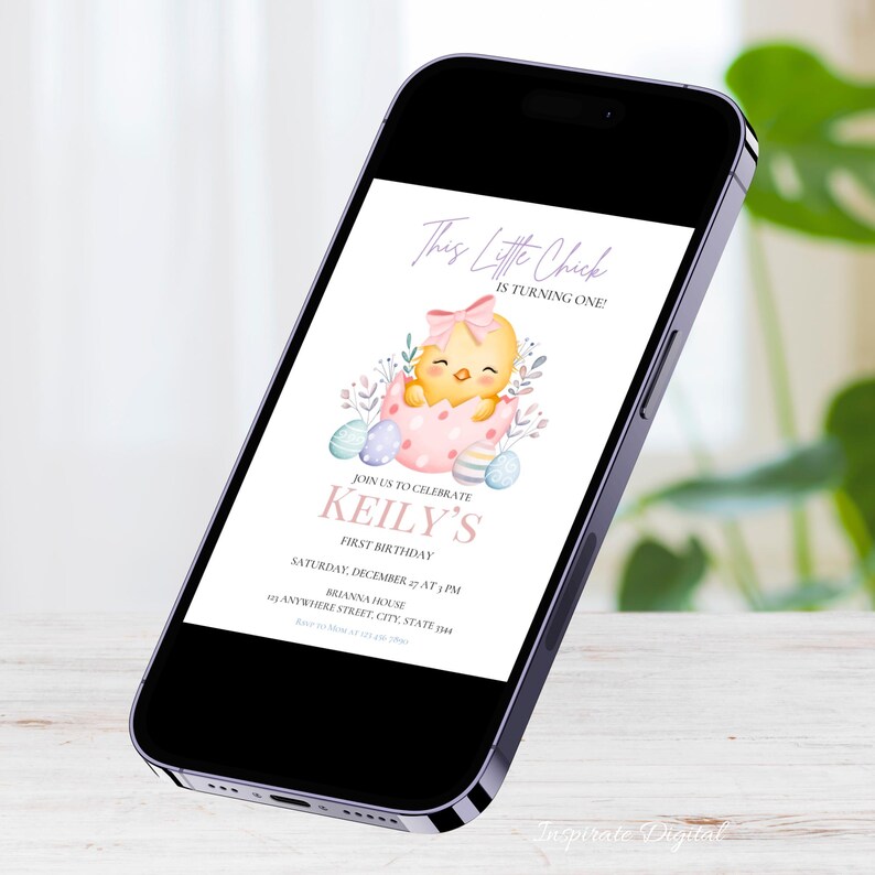 May include: A smartphone displays a digital invitation for a first birthday. The invitation features a watercolor illustration of a yellow chick hatching from a pink egg, surrounded by Easter eggs and foliage. Text includes "This Little Chick is Turning One!" and "Keily's First Birthday".