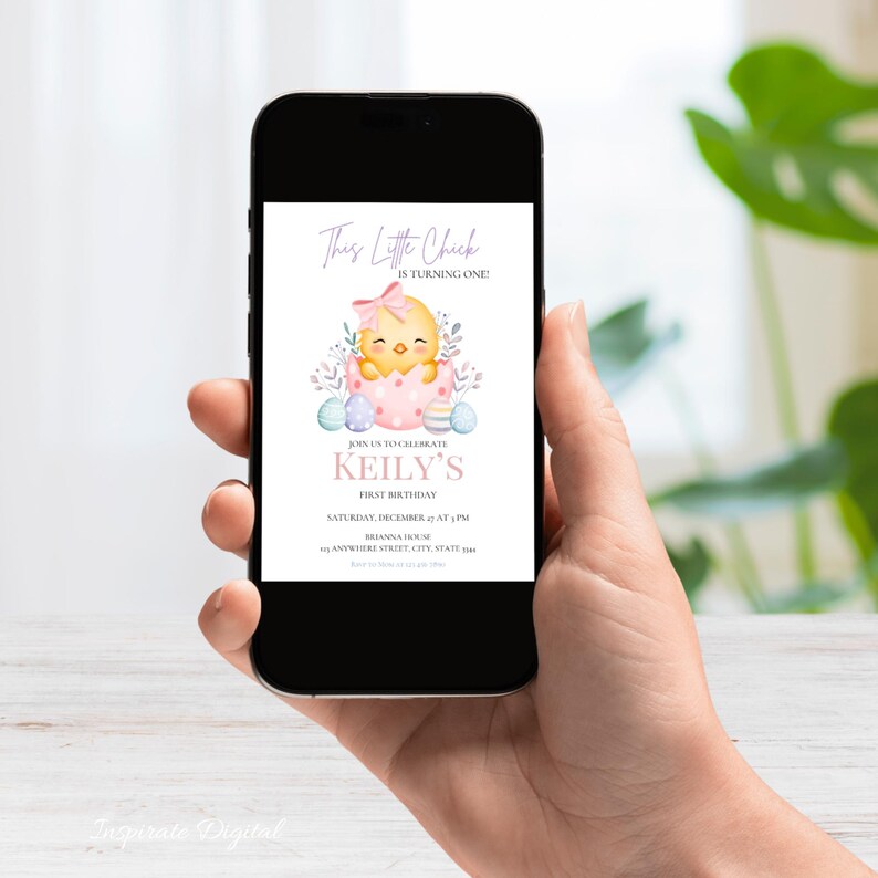 May include: A smartphone displays a digital invitation for a first birthday. The invitation features a watercolor illustration of a yellow chick hatching from a pink egg, surrounded by pastel-colored Easter eggs and floral accents. Text reads "This Little Chick is Turning One!" and details the event.