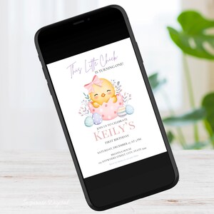 May include: A smartphone displays a digital invitation for a first birthday. The invitation features a watercolor illustration of a yellow chick hatching from a pink egg, with text that reads "This Little Chick is Turning One!" and "Keily's First Birthday."