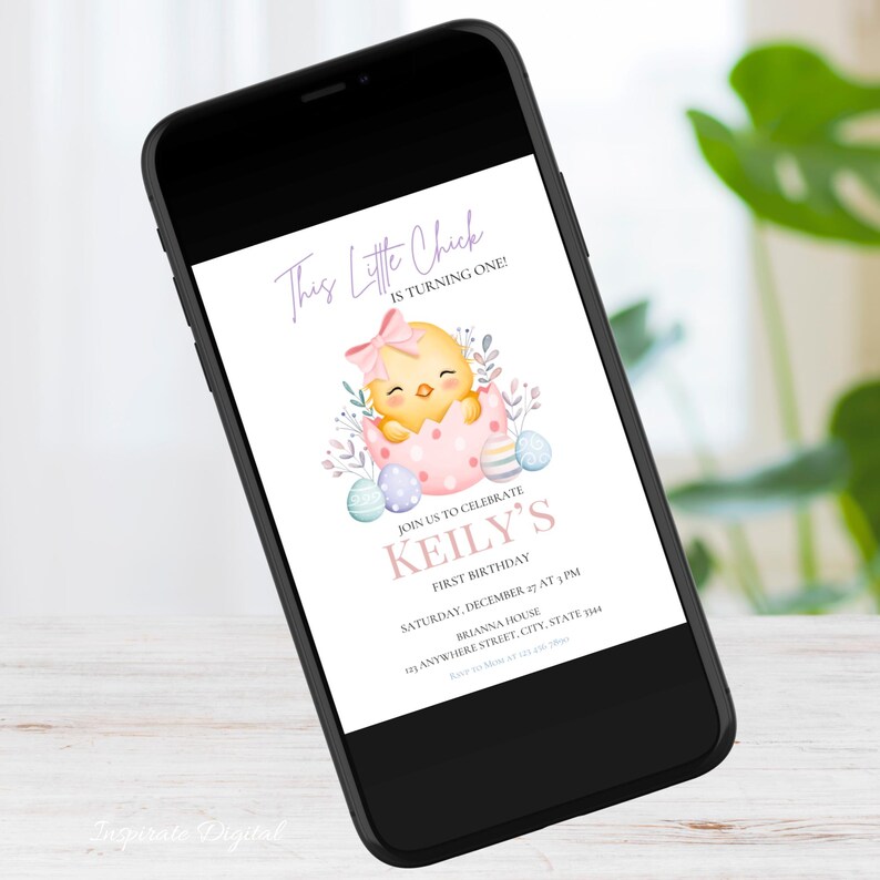 May include: A smartphone displays a digital invitation for a first birthday. The invitation features a watercolor illustration of a yellow chick hatching from a pink egg, with text that reads "This Little Chick is Turning One!" and "Keily's First Birthday."