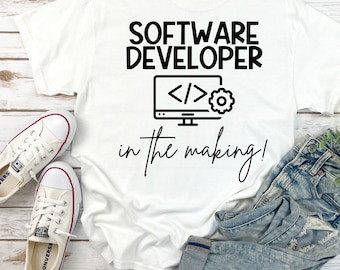 Puede incluir: Camiseta blanca con texto negro que dice "Software Developer in the making!" y un icono negro de un monitor de ordenador con símbolos de código y un engranaje.