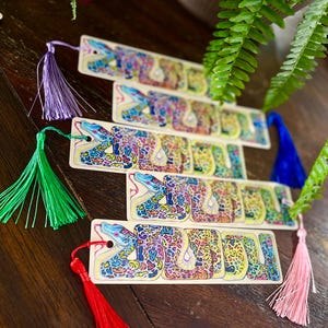 May include: Five colourful bookmarks featuring a detailed illustration of a snake with a bright yellow, blue, green, and red colour scheme. Each bookmark has a tassel attached to the top.