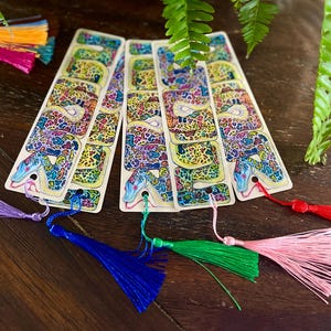 May include: Four colourful bookmarks featuring a detailed illustration of a snake with a colourful, patterned skin. Each bookmark has a tassel attached to the bottom.