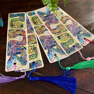 May include: Four colourful bookmarks featuring a detailed illustration of a snake with a patterned skin. Each bookmark has a different coloured tassel.